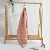 Salmon Poppy muslin swaddle hanging from a rack